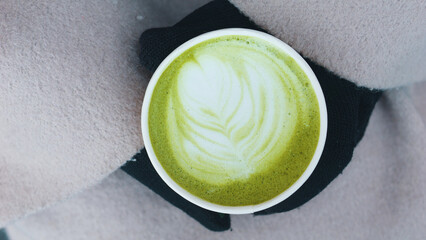 Gloved female hands holding paper cup with green matcha latte. Close up.