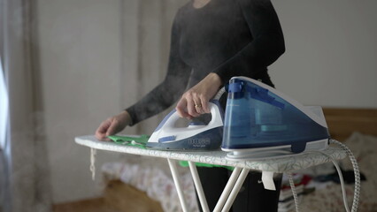 Woman ironing clothes in bedroom, close-up hand holding steam iron doing routine task