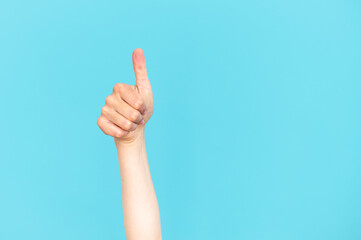 Human hand showing thumb up gesture isolated on blue copy space background