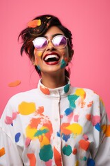 cheerful young woman in sunglasses and shirt with multicolored paint splashes isolated on pink