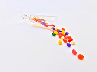 Colorful jellybeans spill from a champagne glass on a white background