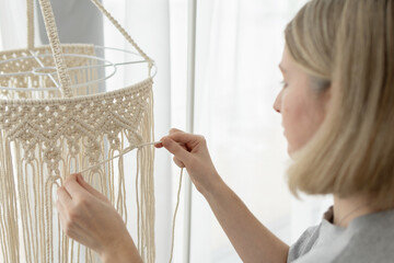 Woman making macrame lampshade using white cord to tie the strings together. Woman knits lampshade...