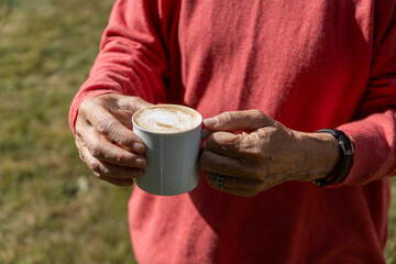 Senior woman enjoying a cup of coffee in the garden, basking in the serenity of nature and savoring the moment.