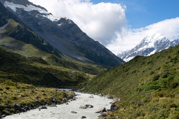 A beautiful breathtaking scene of a massive mountain with a small fresh river melting from glacier near the trekking route at Mount Cook National Park, New Zealand.