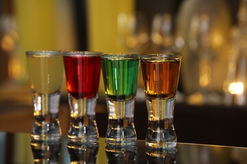 Different shooters in shot glasses on mirror surface against blurred background. Alcohol drink