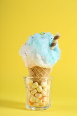 Sweet cotton candy in waffle cone on yellow background