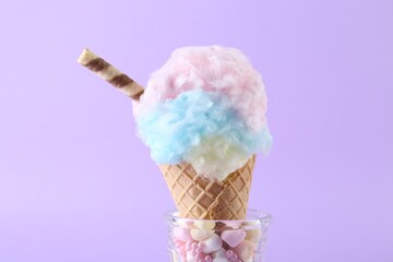 Sweet cotton candy in waffle cone on purple background, closeup