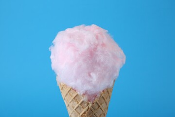 Sweet cotton candy in waffle cone on light blue background, closeup