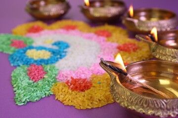 Diwali celebration. Diya lamps and colorful rangoli on purple background, closeup