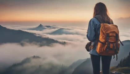 Fotobehang Hipster young girl with backpack enjoying sunset on peak of foggy mountain. © Adi