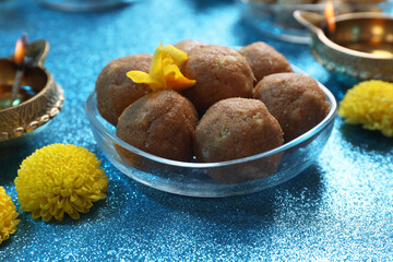 Diwali celebration. Yellow flowers and tasty Indian sweets on shiny light blue table, closeup