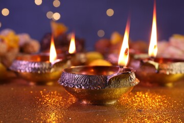 Diwali celebration. Diya lamps on shiny golden table against blurred lights, closeup