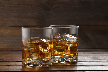 Whiskey with ice cubes in glasses on wooden table, closeup