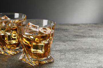 Whiskey and ice cubes in glasses on grey textured table, closeup. Space for text