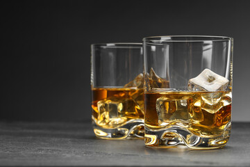 Whiskey and ice cubes in glasses on grey table, closeup. Space for text