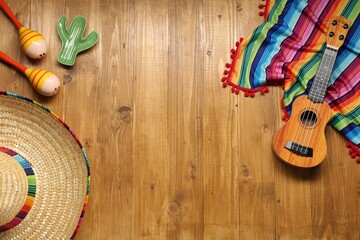 Mexican sombrero hat, maracas, toy cactus, guitar and colorful poncho on wooden background, flat lay. Space for text - obrazy, fototapety, plakaty