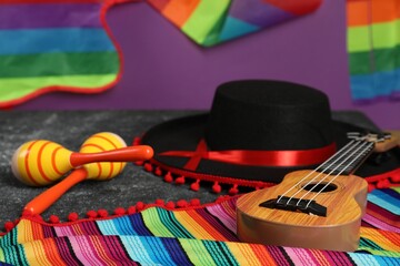 Black Flamenco hat, ukulele, poncho and maracas on dark table, closeup