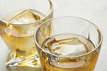 Tasty whiskey with ice in glasses on light table, closeup