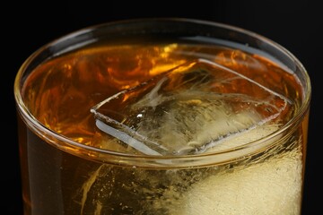 Tasty whiskey and ice in glass on black background, closeup