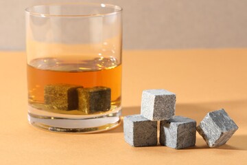 Whiskey stones and drink in glass on orange table, closeup