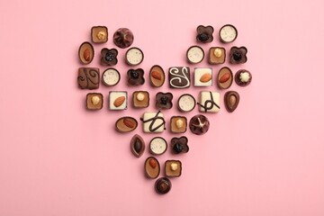 Heart made with delicious chocolate candies on pink background, top view