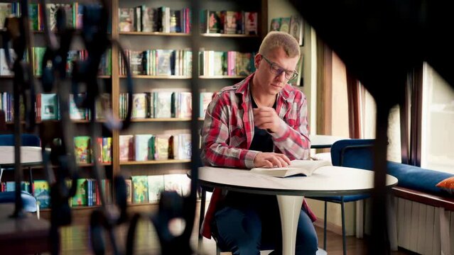male professor in glasses sits in a scientific and technical library reads a book and prepares write a dissertation