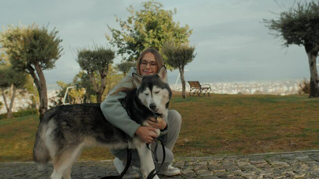 Caring casual woman canine pet owner hugging Husky dog walking at autumn city park landscape closeup