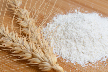 Wheat spikelets and wheat flour close-up on a wooden background.