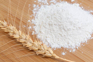 Wheat spikelet and wheat flour on wooden background.