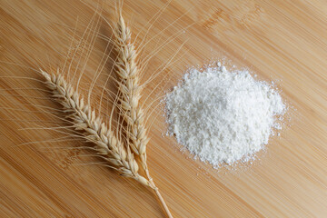 Spikelets and wheat flour next to each other, top view on wooden background.