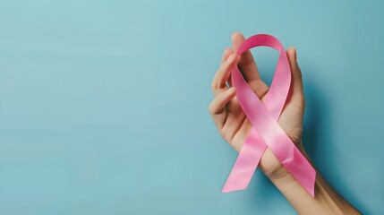 Hand Holding Pink Cancer Ribbon on Blue Background