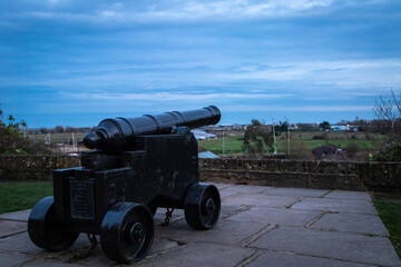 Canon in the Rye castle grounds looking out towards the sea and land in-between, on a cloudy day just after sunset 