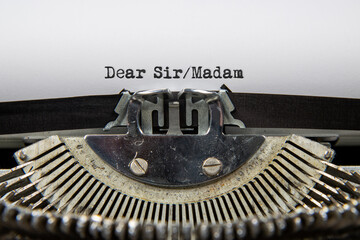 A close up of an old fashioned typewriter that has printed out the words Dear Sir Madam