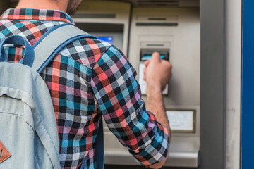 Young man put his credit card at the ATM on a city street.