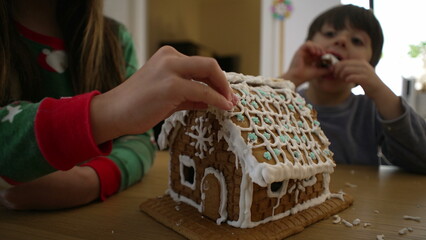 Children taking apart gingerbread home covered in royal ice, siblings brother and sister eating...