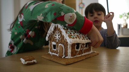 Children taking apart gingerbread home covered in royal ice, siblings brother and sister eating...