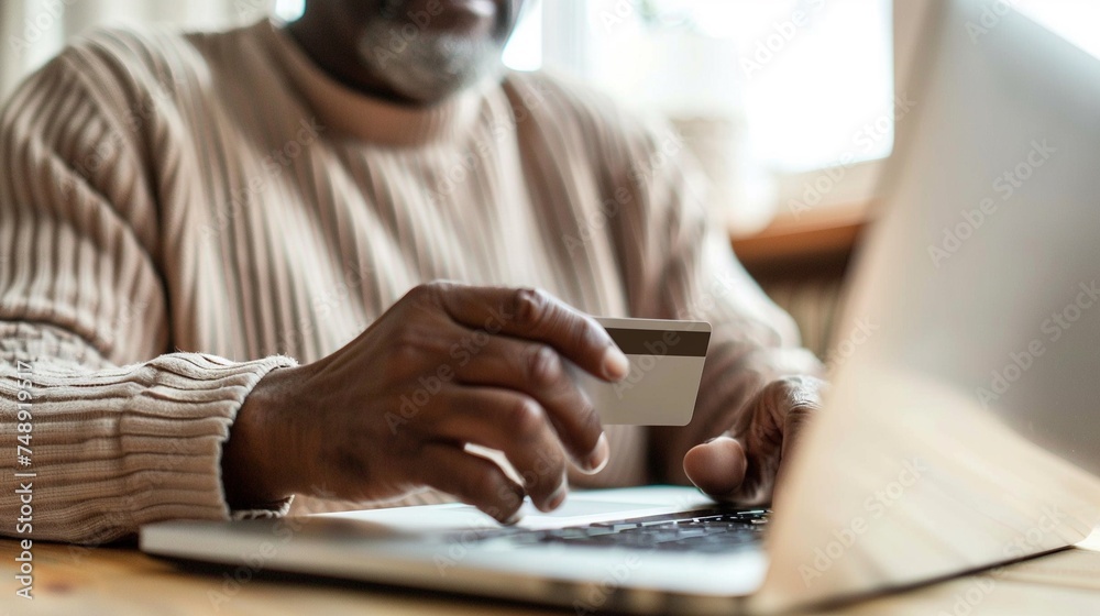 Wall mural Elderly African American man enters his credit card information online via his laptop connected to the internet. Many elderly ones are vulnerable to online scams - Wall murals