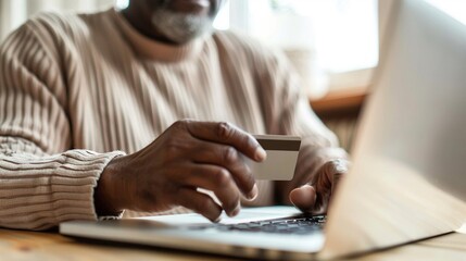 Elderly African American man enters his credit card information online via his laptop connected to the internet. Many elderly ones are vulnerable to online scams - obrazy, fototapety, plakaty