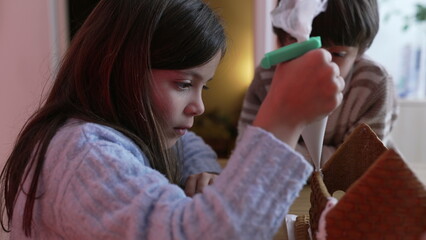 Little girl applying royal ice into gingerbread home decoration. Family preparing for traditional...