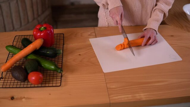 2.	Close-up video of a young woman preparing food in a rustic kitchen, she is carefully chopping a carrot using a sharp knife on a chopping board placed over a hard wood kitchen top.