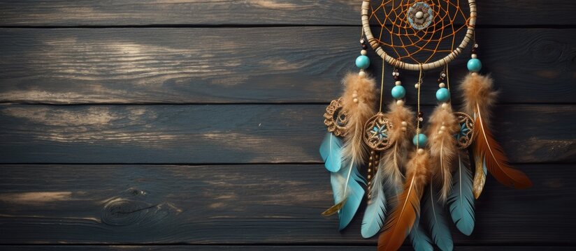 A handmade brown and blue dream catcher adorned with feathers, threads, and beads is hanging on a wooden wall.