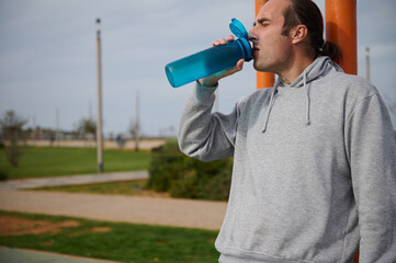 A sportsman drinking water from the bottle, hydrating and resting after heavy workout on the urban...