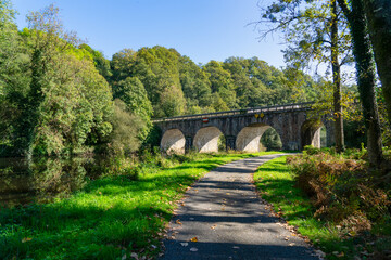 Fototapeta premium Un pont de pierre majestueux enjambe le Blavet, tandis qu'un chemin sinueux invite à l'aventure le long de ses rives verdoyantes, révélant la beauté naturelle du Morbihan breton.