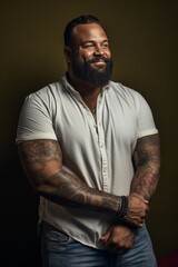 A confident man with a beard and tattoos standing in front of a dark background, showcasing his scars and imperfections