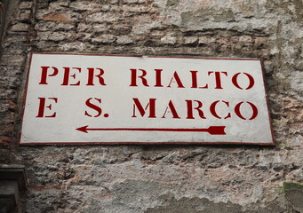 road sign in the wall in Venice in Italy with text to go at Rialto Bridge or in Saint Mark Square