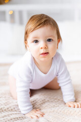 a close-up portrait of a cute little child in a bright room in white clothes at home on a bed, the concept of children's goods