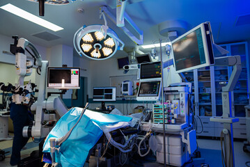 A hospital room with a patient on a table and a doctor standing behind him. The room is brightly lit and has several monitors and medical equipment