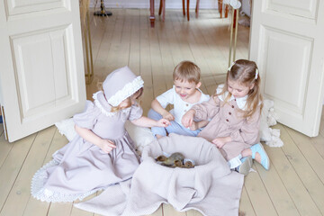 Obraz na płótnie Canvas three children little blonde girls in vintage dress and cute little boy in living room country house on spring day playing with baby ducks ducklings, happy childhood, simple cozy life, happy Easter