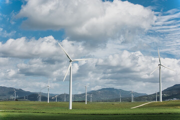 Sustainable energy production: Wind turbines against a cloudy sky on a green field - 748946767