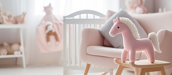 A pink toy horse is placed on a wooden rocking chair in a simple baby room interior. The white rocking horse stands in front of a cradle with a pink blanket.
